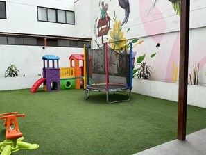 A children's play area with a trampoline and colorful play structures on artificial grass. - APT VIZUALE - LINCE (Lima)