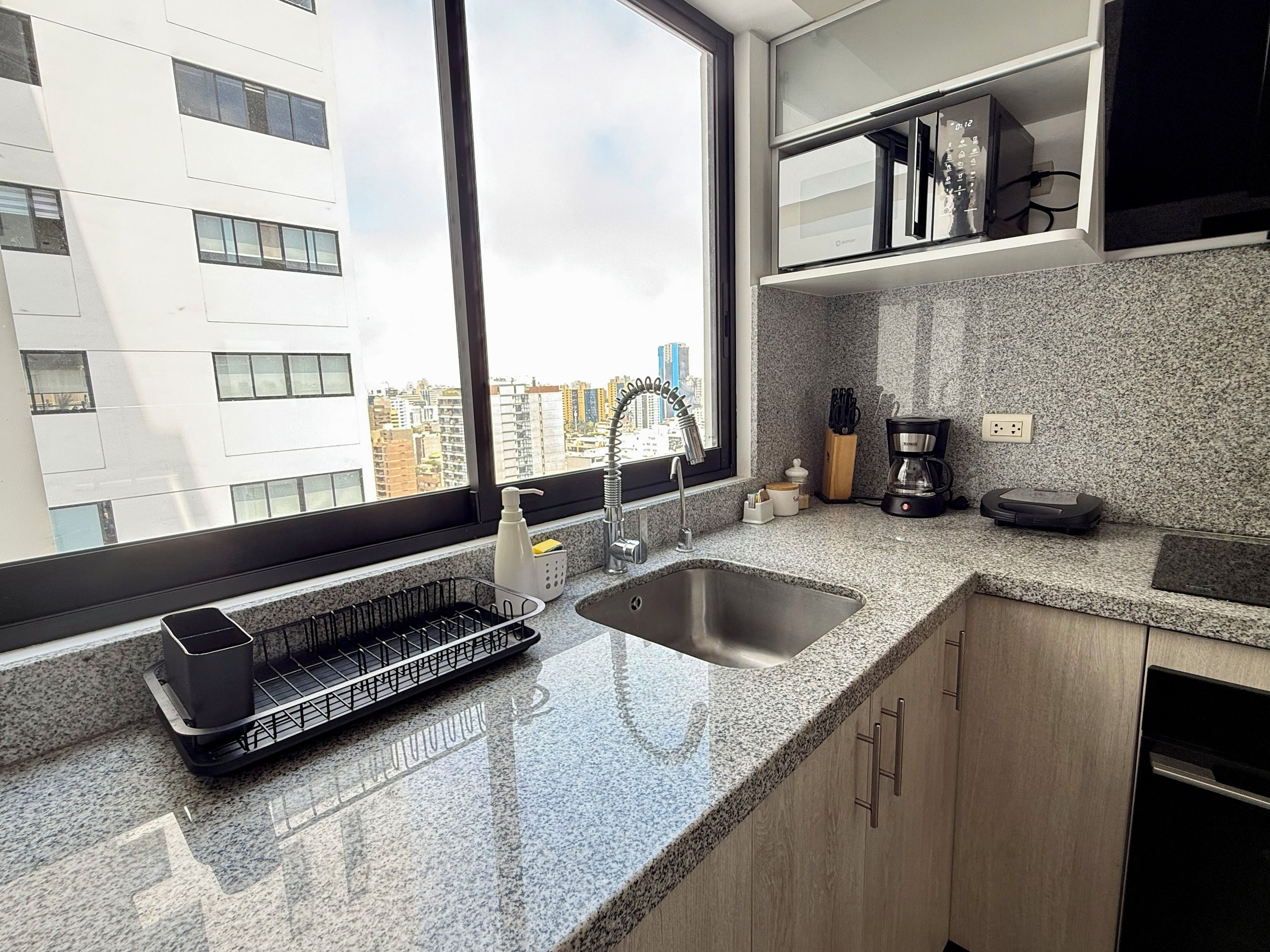 Una cocina moderna con encimera de granito, pileta de acero inoxidable y cafetera.