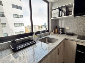 A modern kitchen with a granite countertop, stainless steel sink, and a coffee maker. - APT VIZUALE - LINCE (Lima)