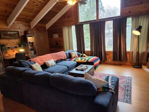 Una habitación acogedora de estilo cabaña con un amplio sofá modular, una mesita pequeña y una ventana con cortinas.