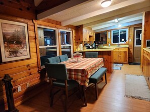 Acogedor interior de cabaña con mesa de comedor, sillas, armarios de madera y zona de cocina.