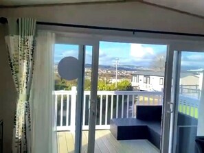 Un balcón con vista a una zona residencial, barandilla blanca y puerta que da al interior.