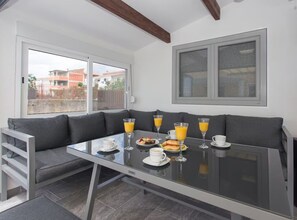 Ein Frühstücksaufenthalt mit einem Glastisch, einem grauen Sofa und Blick auf Gebäude.