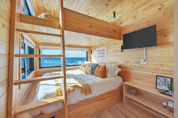 A wooden cabin bedroom with a bunk bed, a television, and a view of the sea. - Direct Waterfront Cabin Sunset Views 6 (Fort Walton Beach)