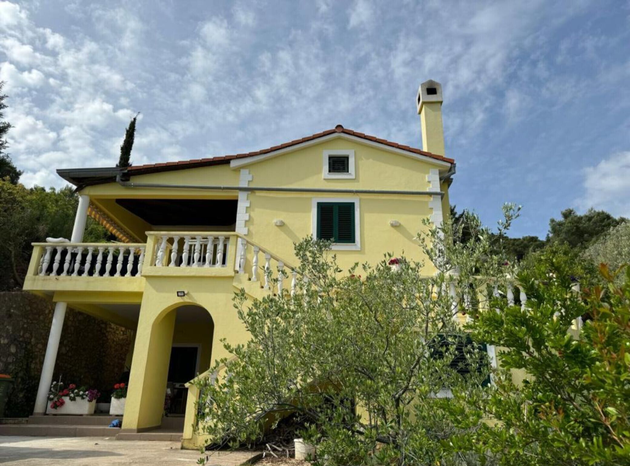 A two-story building with a yellow facade, a balcony with white balustrades, and a chimney.