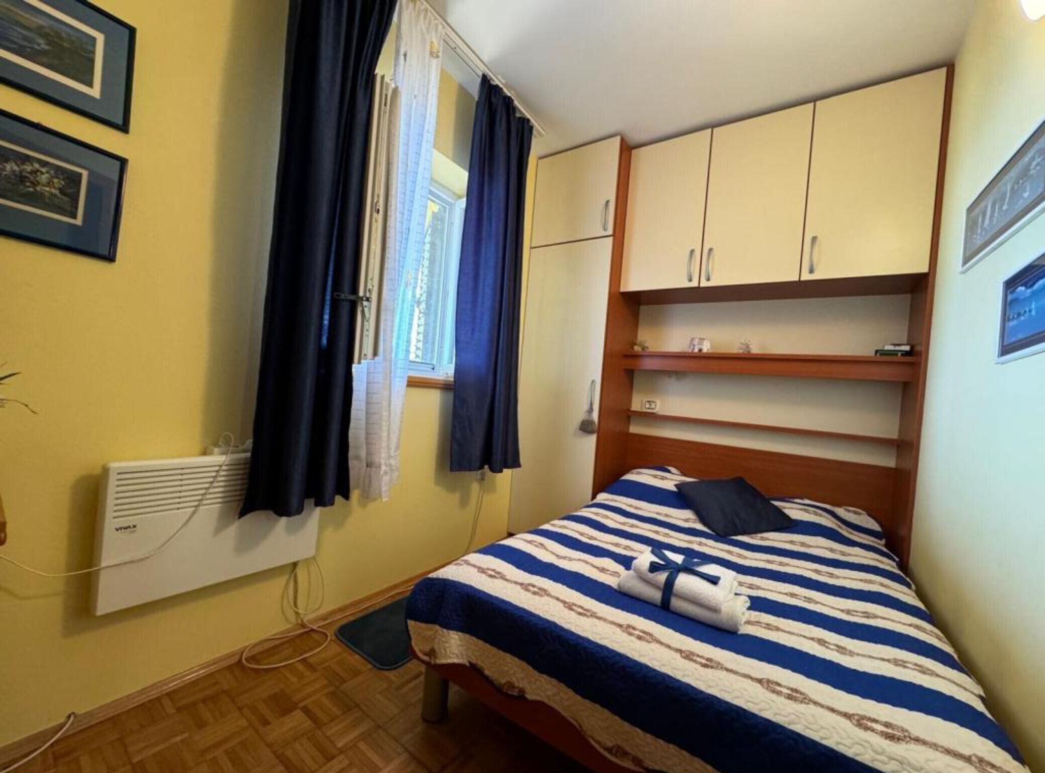 A small bedroom with a bed, a radiator, a window with curtains, and a wooden wardrobe.