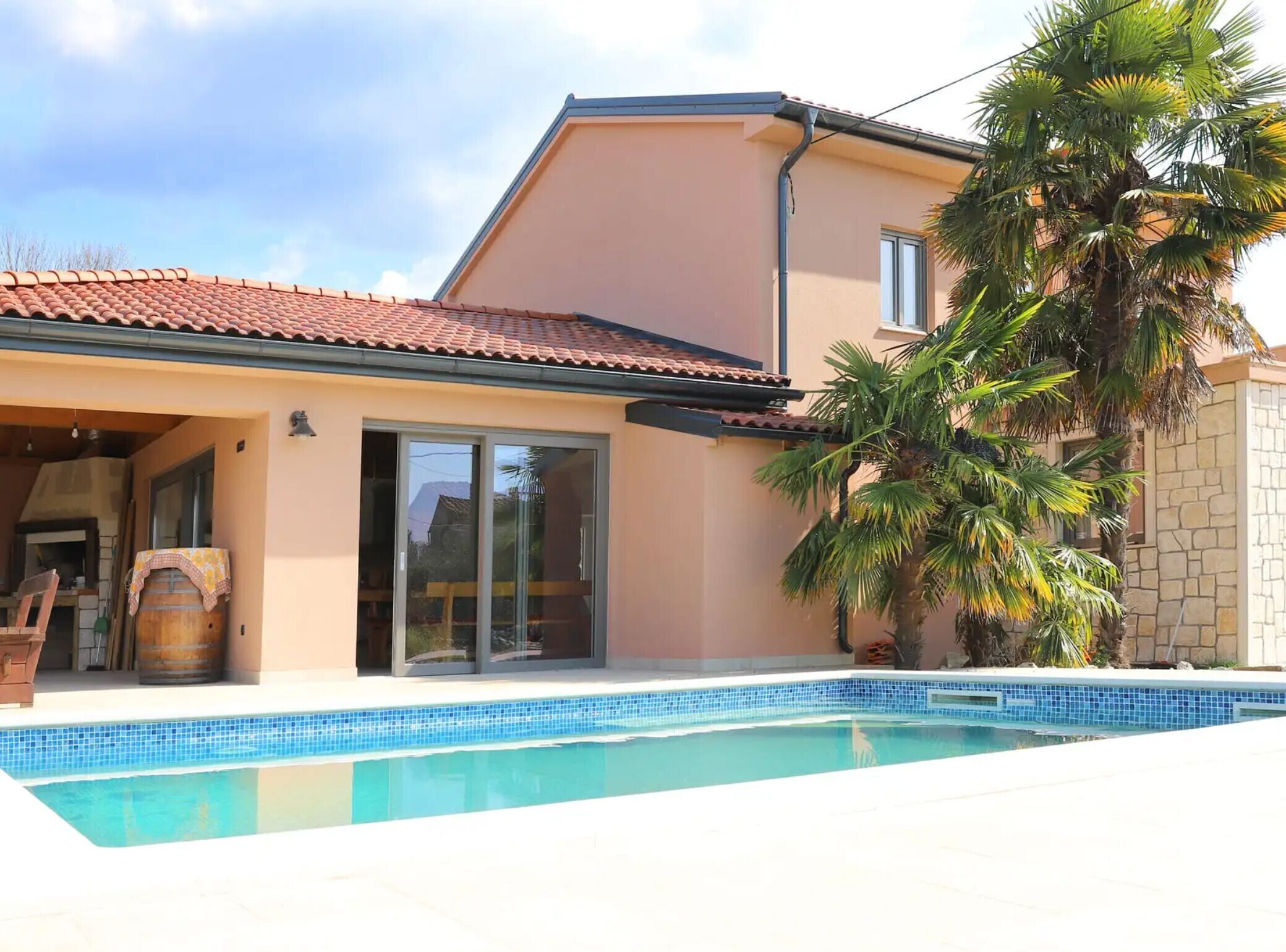 Une maison avec une piscine, un toit en tuiles et un palmier.