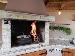 Ein Kamin aus Stein im Freien mit Feuer, umgeben von einem gefliesten Boden und einer hölzernen Bank.