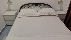 Un letto con biancheria bianca, una testiera in metallo nero e due comodini con lampade.