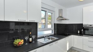 A modern kitchen with white cabinets, black countertops, a built-in oven, and a window providing natural light. - Adriatic Villa Privlaka - Two bedroom Villa with pool (Privlaka)