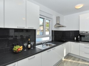 A modern kitchen with white cabinets, black countertops, a built-in oven, and a window providing natural light. - Adriatic Villa Privlaka - Two bedroom Villa with pool (Privlaka)