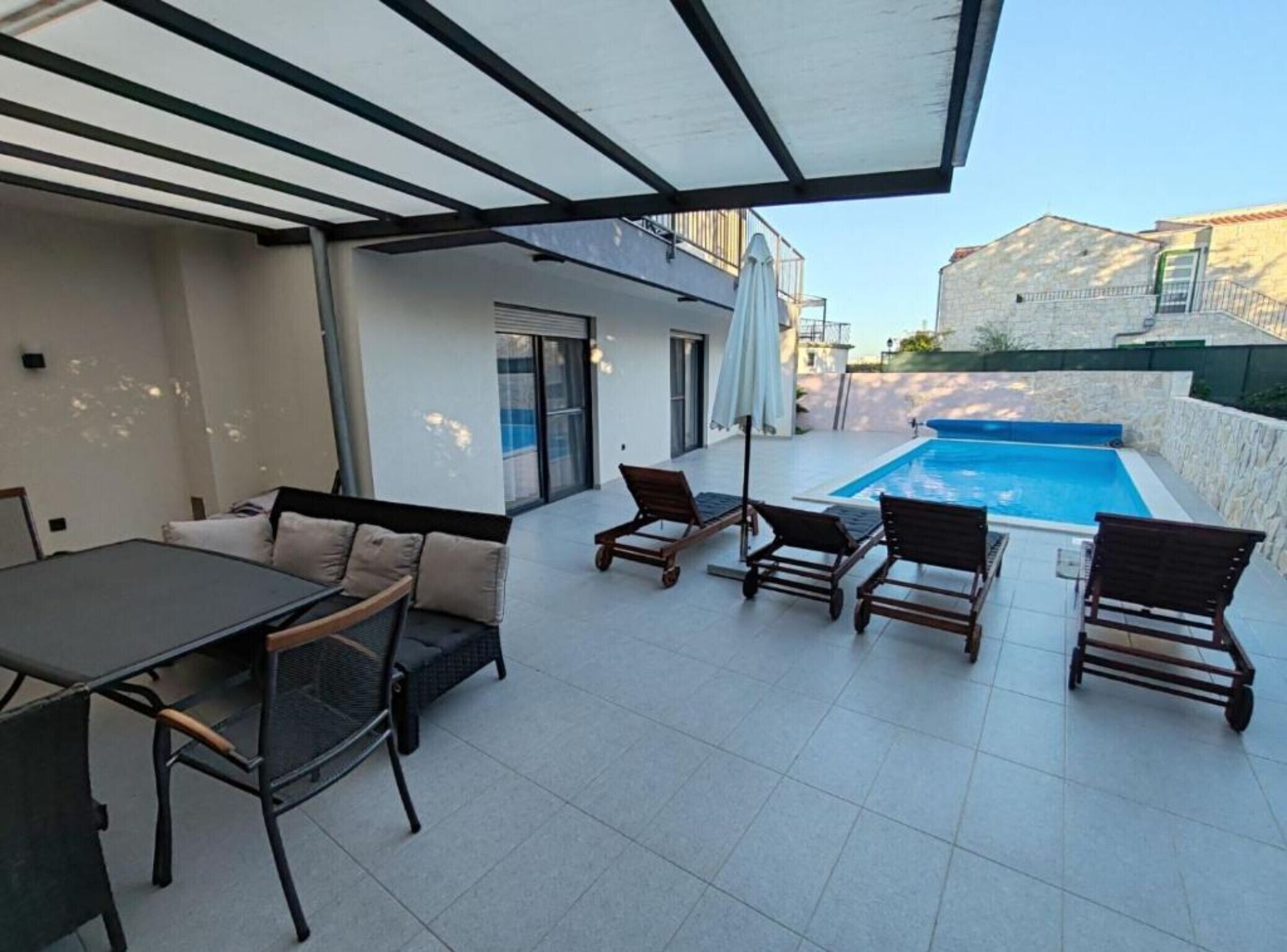 A covered outdoor area with a pool, a dining table, and lounge chairs.