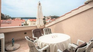 Un balcon avec une table ronde et des chaises, donnant sur une ville où les bâtiments ont des toits rouges et qui est bordée par un plan d’eau.