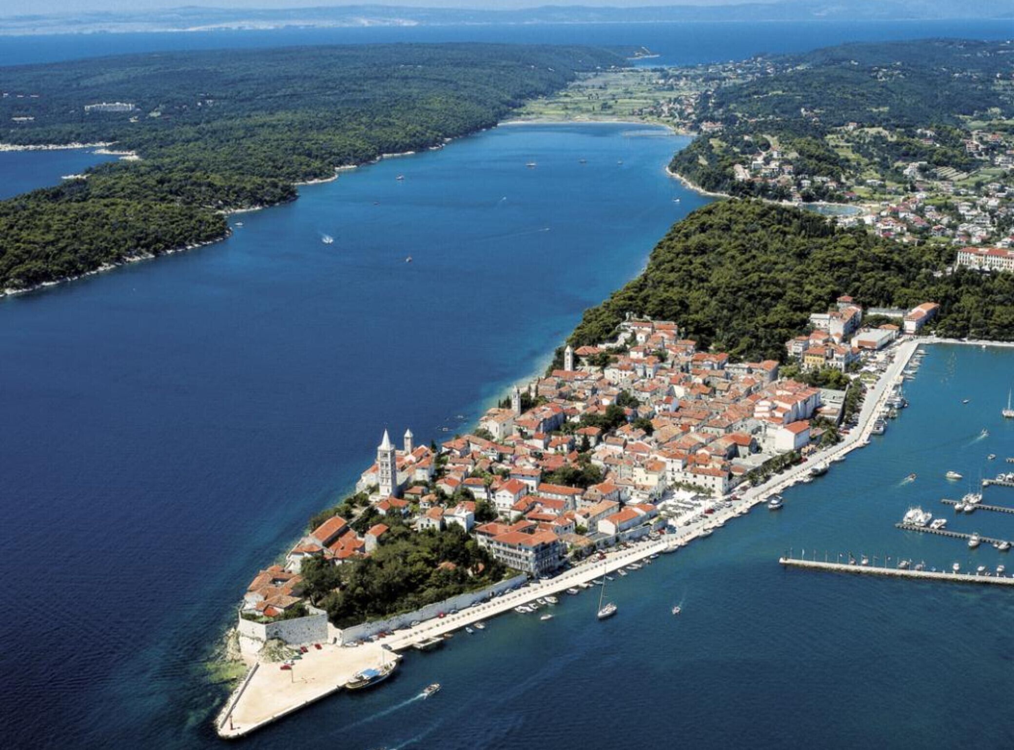 An aerial view of a coastal town with a dense cluster of buildings, a prominent church, and a marina with boats.