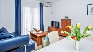 Una sala de estar moderna con un sofá azul, una mesa de centro de madera con un frutero, un televisor sobre un mueble de madera y un jarrón con tulipanes.