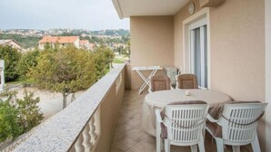 Un balcón con mesa y sillas, una ventana y vistas a un pueblo y colinas.