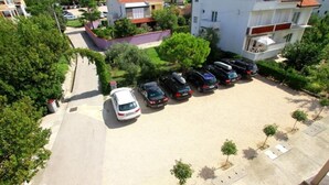 Oversigtsbillede af et boligområde med en række parkerede biler, en hvid bygning med rødt tag og grøn bevoksning omkring.