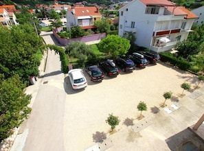 Une vue aérienne d’un quartier résidentiel, avec une rangée de voitures garées, un bâtiment blanc doté d’un toit rouge et une végétation luxuriante tout autour.