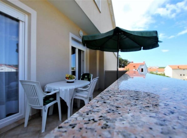 Un espace extérieur aménagé pour prendre les repas, avec une table et des chaises, un saladier rempli de fruits et un parasol vert.