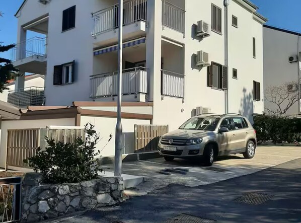 Un edificio de dos pisos con balcones, un coche aparcado y un muro de piedra.