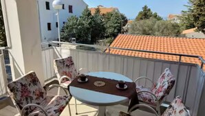 Ein Balkon mit Tisch und Stühlen, der auf einen Wohnbereich mit roten Ziegeldächern und Bäumen blickt.