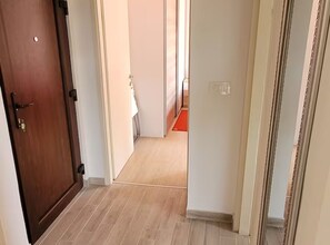 A narrow hallway with a wooden door on the left, a white wall on the right, and a red mat on the floor. - Apartment Punat Buka - Two Bedroom Apartment with Terrace (Punat)