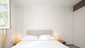 Un dormitorio minimalista con una cama grande, dos lámparas de noche y una toalla doblada sobre la cama.