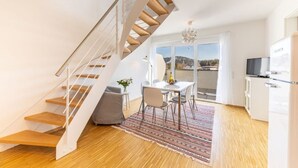 A modern interior with a wooden staircase, a dining area with a table and chairs, and a kitchen area. - Ferienresidenz Hinterzarten FEWO H12 (Hinterzarten)