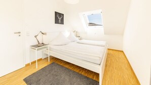 Un dormitorio con una cama, una mesita de noche con lámpara, un cuadro en la pared y una ventana.