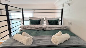 A single bed with a green quilt, two pillows, and two rolled towels. - Cozy Apartment 3 min from Main Station Old Town Quiet Dapartments.eu (Kraków)