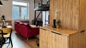 A compact living space with a red sofa, wooden flooring, a black staircase, and a small dining area with a table and chairs. - Cozy Apartment 3 min from Main Station Old Town Quiet Dapartments.eu (Kraków)