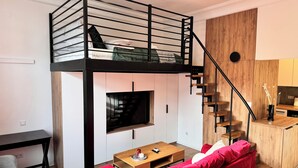 A loft-style bedroom with a bunk bed, a wooden staircase, a TV, a red sofa, and a small wooden table. - Cozy Apartment 3 min from Main Station Old Town Quiet Dapartments.eu (Kraków)