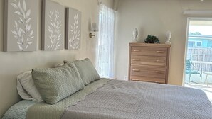 Ett sovrum med en säng, en byrå, en lampa och ett fönster med utsikt över omgivningen.