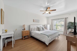 A bedroom with a bed, desk, chair, nightstand, lamp, ceiling fan, window with curtains, and a plant. - Sunny Naples Getaway- 2BR Condo with Pool, Tennis, & Minutes to Beach (Naples)