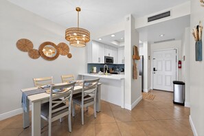 A modern kitchen with white cabinets, a central island, and a dining area with a table and chairs. - Sunny Naples Getaway- 2BR Condo with Pool, Tennis, & Minutes to Beach (Naples)