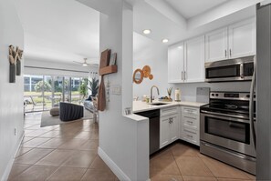 A modern kitchen with white cabinets, stainless steel appliances, and a large window. - Sunny Naples Getaway- 2BR Condo with Pool, Tennis, & Minutes to Beach (Naples)