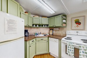 A kitchen with green cabinets, a white refrigerator, a coffee maker, a sink, and a stove. - Tranquil Banner Elk Escape | Views, Pool & Slopes (Banner Elk)