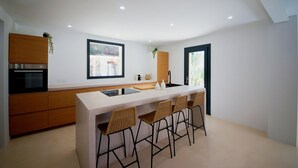 Una cocina moderna con una isla central, taburetes de bar, armarios de madera y vistas a un puente a través de una ventana.