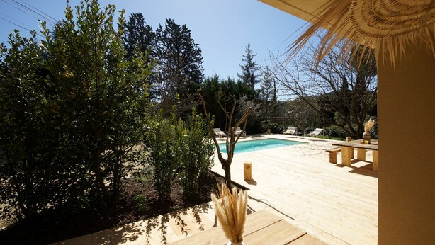 Una terraza de madera con piscina, rodeada de vegetación y una estructura de techo de paja.