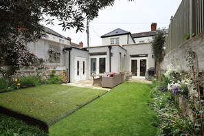 A residential backyard with a lawn, outdoor furniture, and a house with a grey facade and a chimney. - Luxurious and spacious  3-bedroom house in central Dublin neighborhood (Dublin)