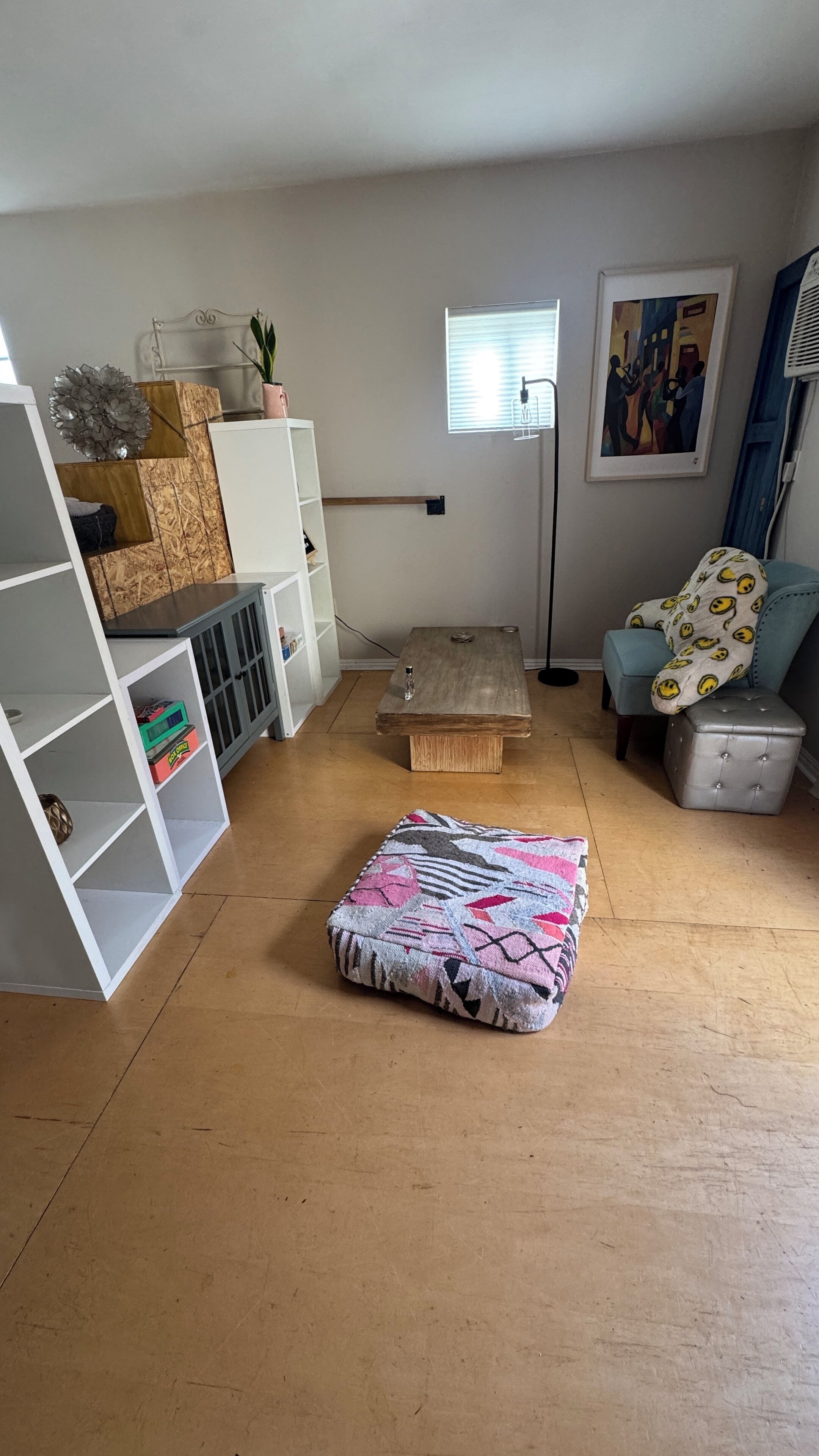 Tunnelmallinen olohuone, jossa on puulattia, kuviollinen rahi, valkoinen hyllykkö, pieni puupöytä ja sininen tuoli.