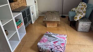 A cozy living room with a wooden floor, a patterned ottoman, a white shelving unit, a small wooden table, and a blue chair. - Adorable bungalow with AC in charming Glendale perfect for relaxing (Glendale)