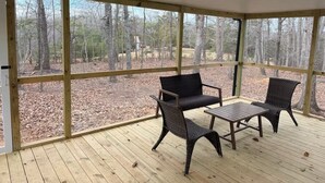 Un'area esterna coperta con pavimento in legno e ampie finestre, con due poltrone in vimini e un tavolino.