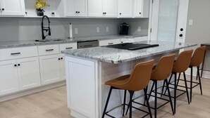 Cucina moderna con mobili bianchi, un piano di lavoro in granito e una zona bar con quattro sgabelli.