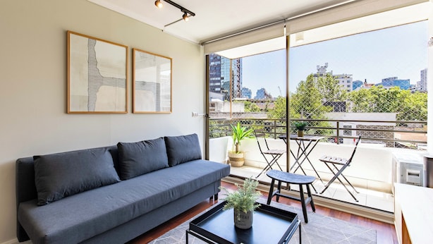 A modern living room with a grey sofa, a coffee table with a plant, and a balcony with a table and chairs. - 2-bedroom apartment in peaceful Providencia with AC and charm (Providencia)