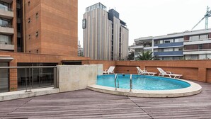 A rooftop pool area with a wooden deck, lounge chairs, and a view of surrounding buildings. - 2-bedroom apartment in peaceful Providencia with AC and charm (Providencia)
