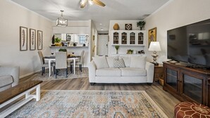 A living room with a sofa, a TV, a ceiling fan, a dining area with a table and chairs, and a kitchen in the background. - Canyon Lake Retreat w Deck, Grill & Deer Views! (Canyon Lake)