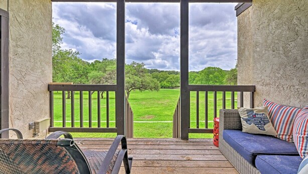 A covered porch with a view of a grassy field, a wicker chair, a blue sofa with pillows, and a wooden railing. - Canyon Lake Retreat w Deck, Grill & Deer Views! (Canyon Lake)