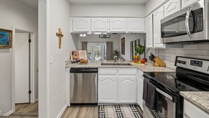 A modern kitchen with white cabinetry, a stainless steel dishwasher, a microwave, and a black stove. - Canyon Lake Retreat w Deck, Grill & Deer Views! (Canyon Lake)
