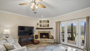 A living room with a fireplace, television, and a view to the outdoors. - Canyon Lake Retreat w Deck, Grill & Deer Views! (Canyon Lake)